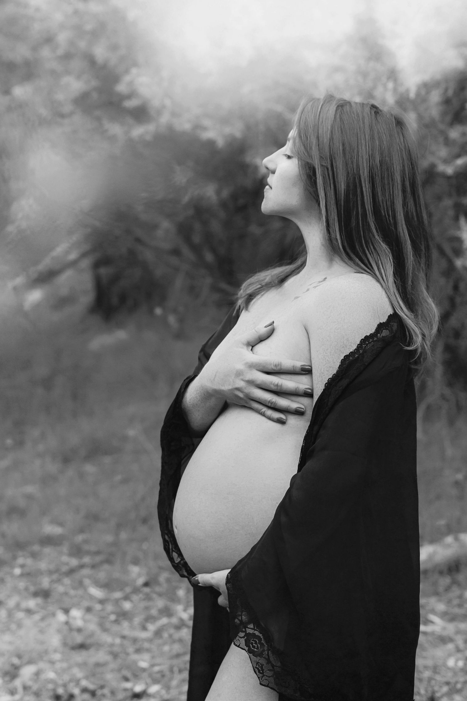 Black and white maternity portrait with dramatic cloudy sky background.