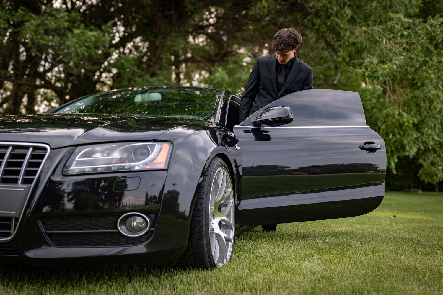 a young man in a tux getting into a black car.