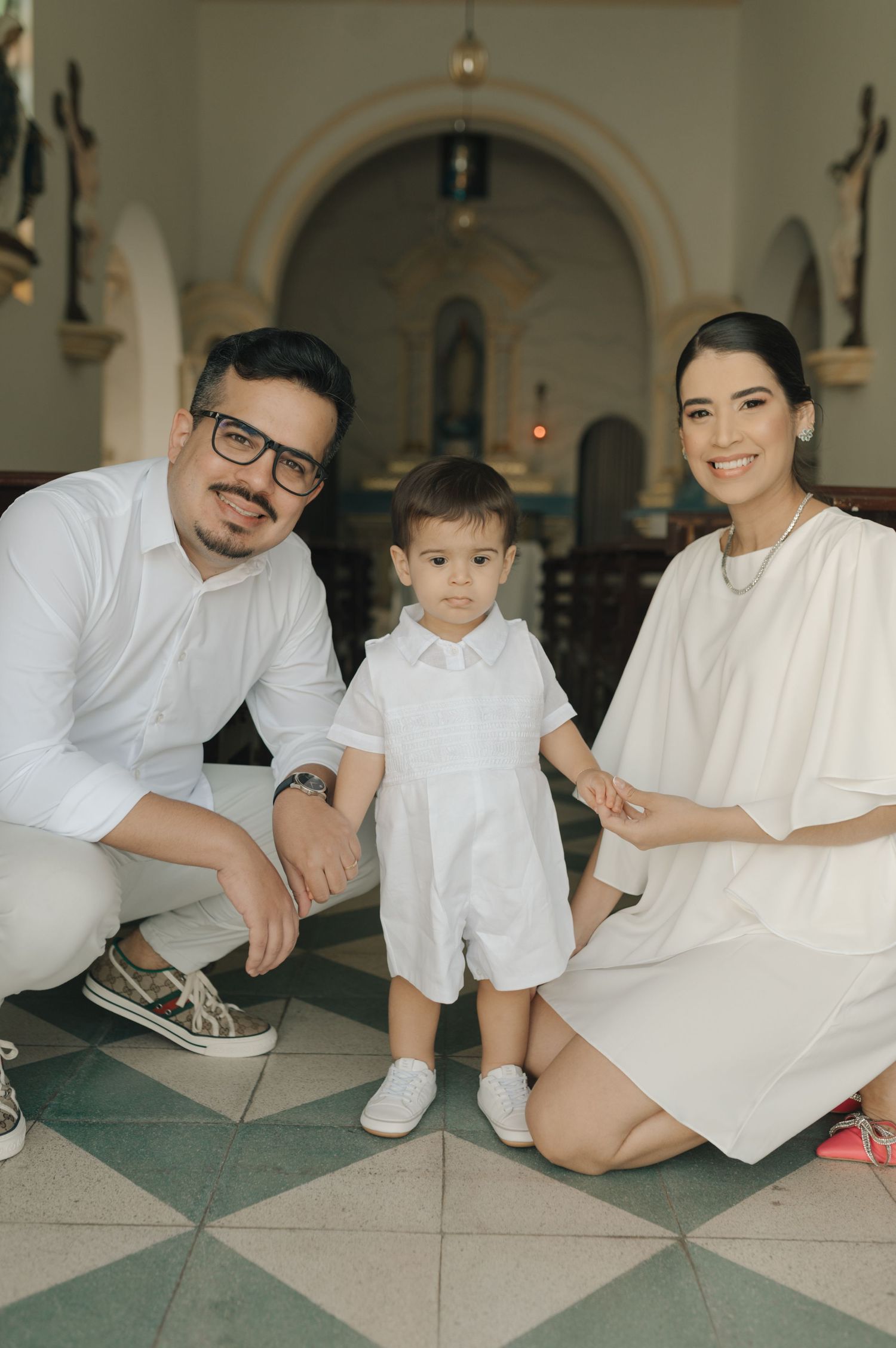 Family portrait in white attire inside church with checkerboard floor and arched doorway.