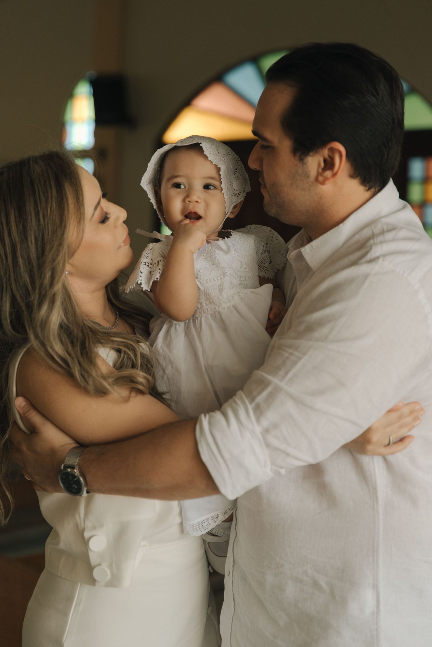 A tender family moment with baby in traditional white baptismal gown inside a church.