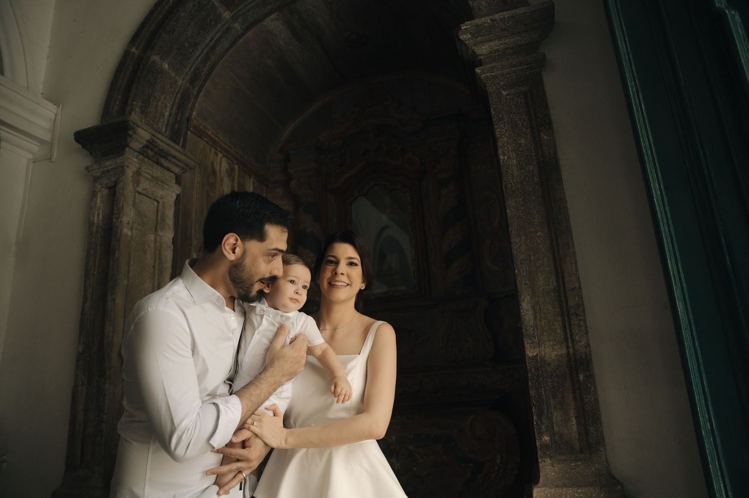 A couple in wedding attire embraces in an elegant stone archway setting during their romantic photoshoot.