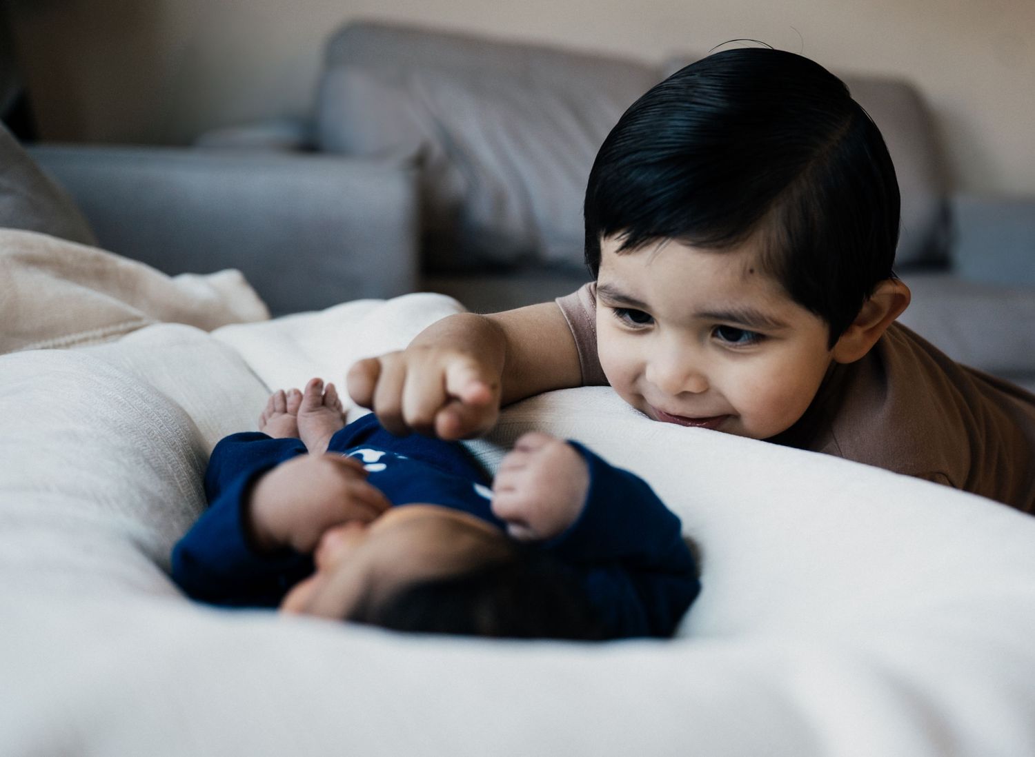 Someone playing with a blue stuffed animal while lying comfortably on a white bed.