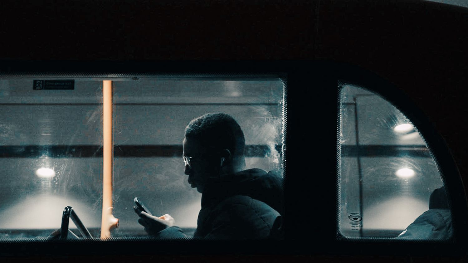 Silhouette of passenger using phone inside dimly lit public transit vehicle at night.