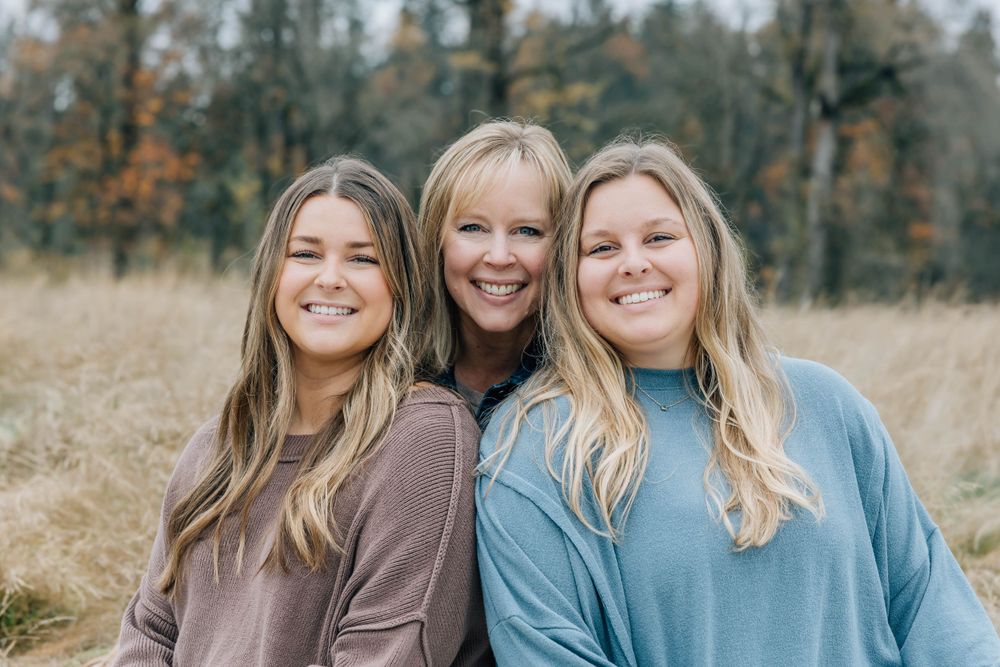 Three smiling women with blonde hair posing together in an autumn field.