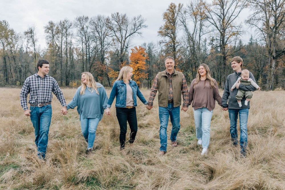 Family of seven walking hand-in-hand through a golden autumn meadow.