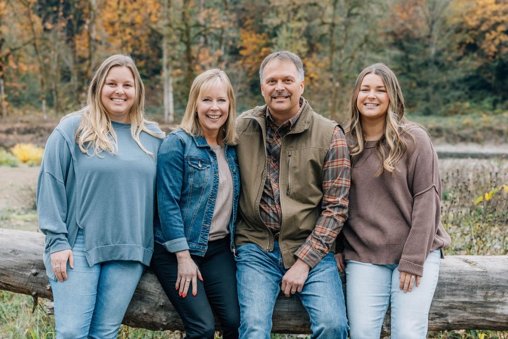 Family of four smiling together on a log in a colorful autumn outdoor setting.