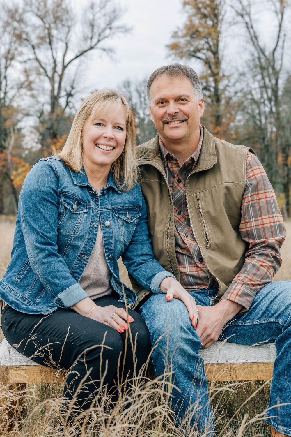 Smiling couple sitting together outdoors in a field of tall dry grass during autumn.