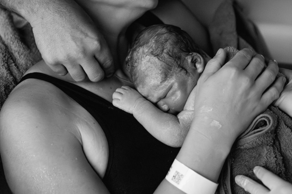 Black and white image of newborn baby resting on mother's chest after just being born in hospital.