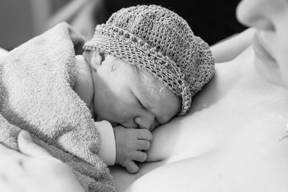 A peaceful newborn wearing a knit cap sleeps while wrapped in a cozy towel.