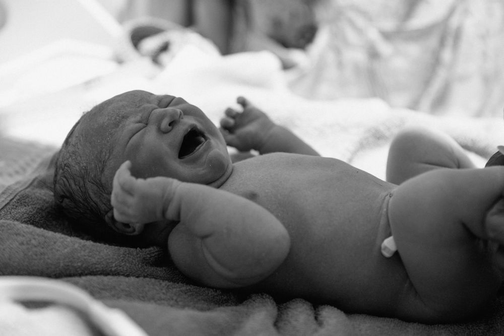 Black and white capture of a crying newborn lying on a hospital blanket.