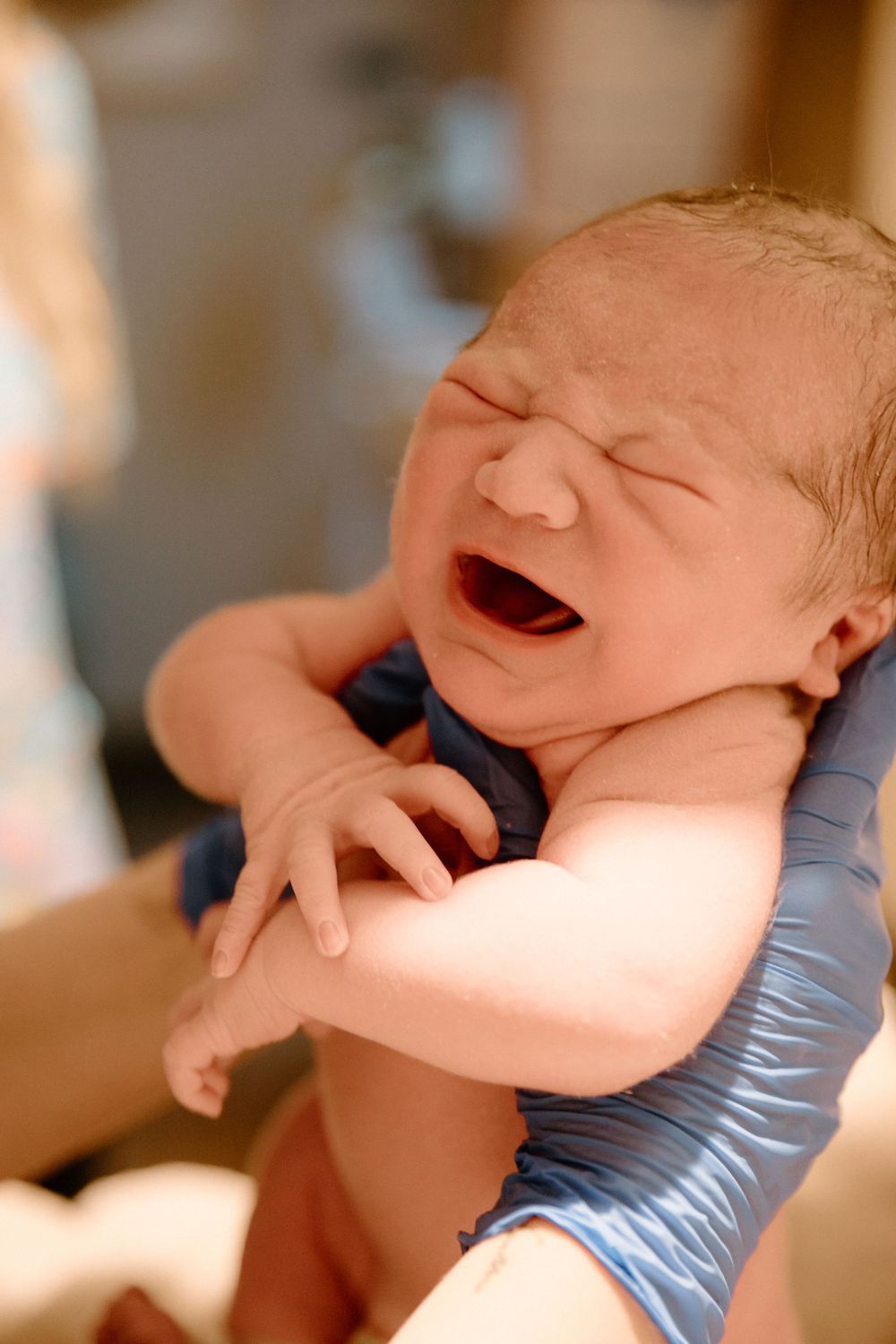 A crying newborn being held and examined in a medical setting.