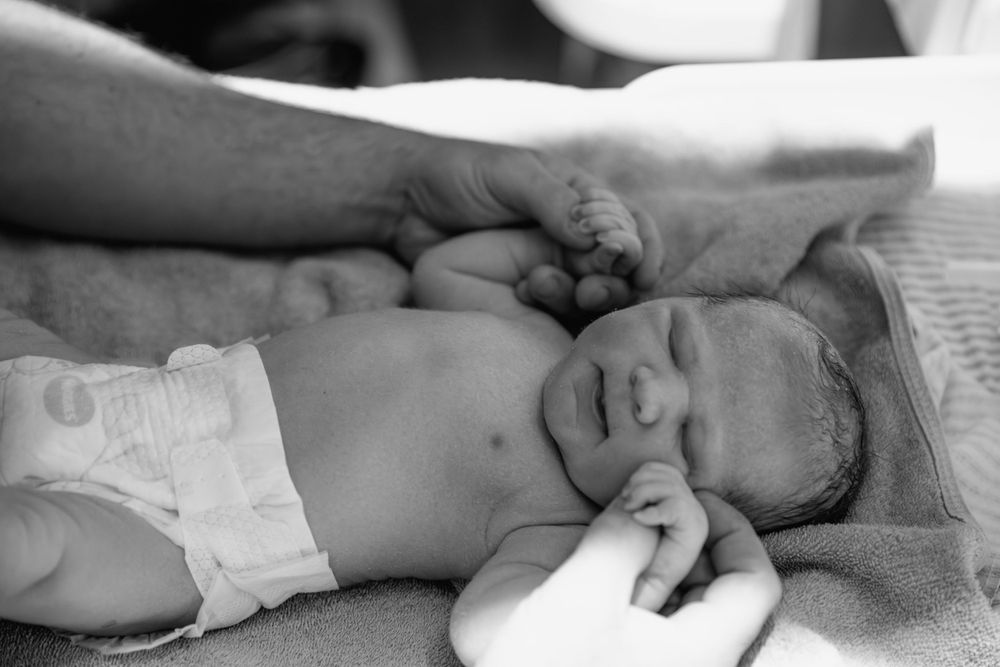 A newborn baby lies on their back with outstretched arms in a black and white photograph.