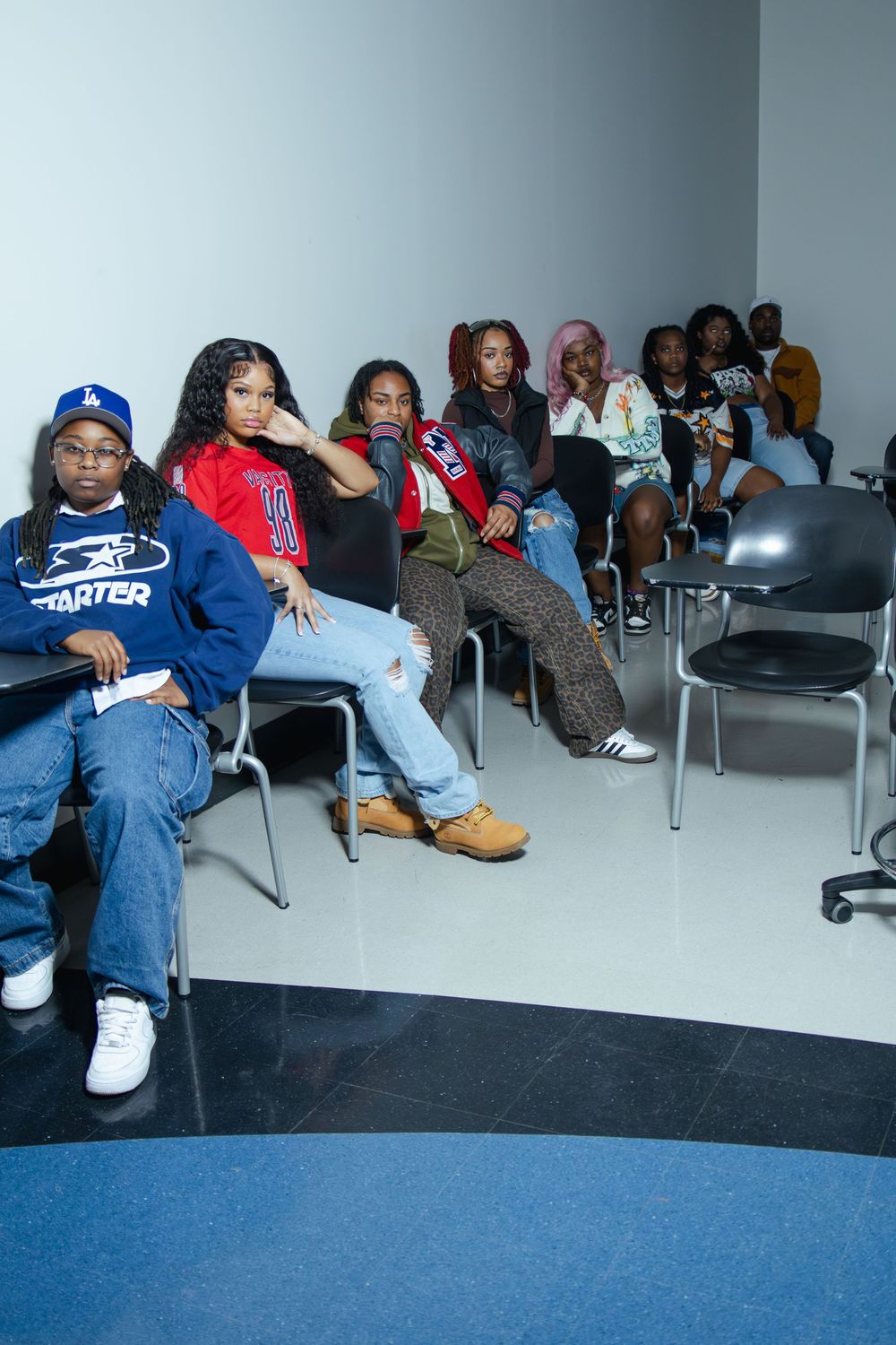 Group of people sitting casually in chairs against white wall in indoor space.