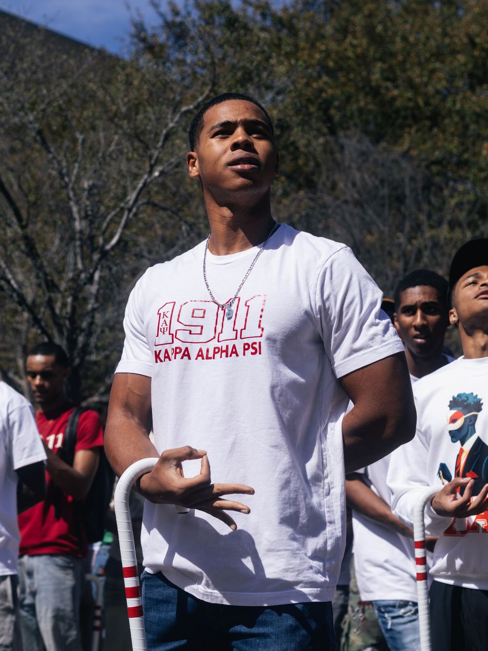 Group wearing white shirts with Greek letters performing coordinated movements outdoors.