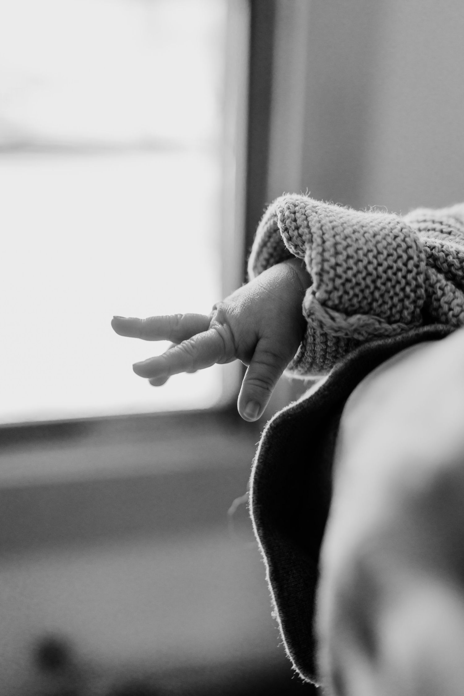 Black and white close-up of a baby's tiny hand reaching out from under a knitted blanket.