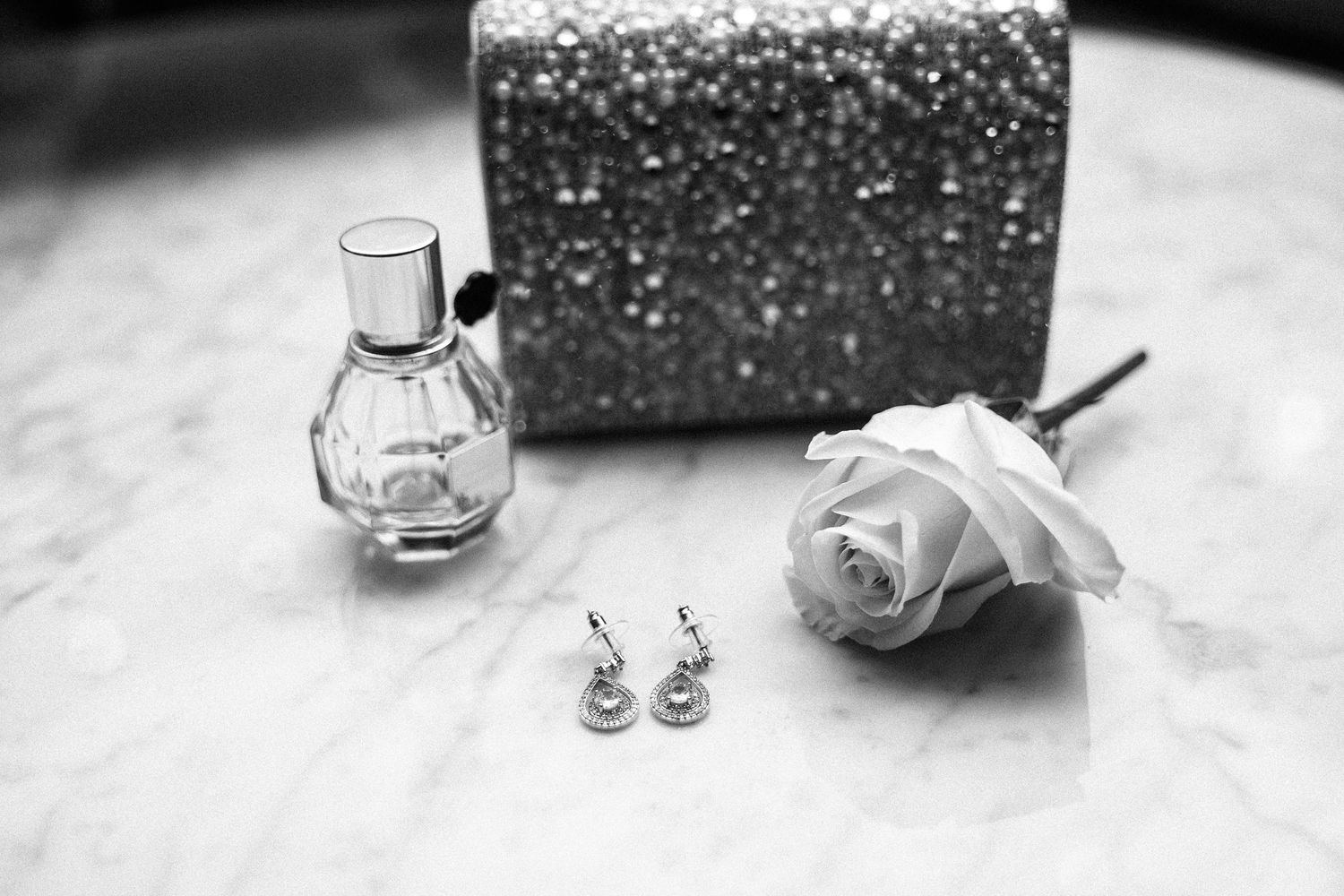 Wedding accessories including perfume bottle, earrings and white rose on table.