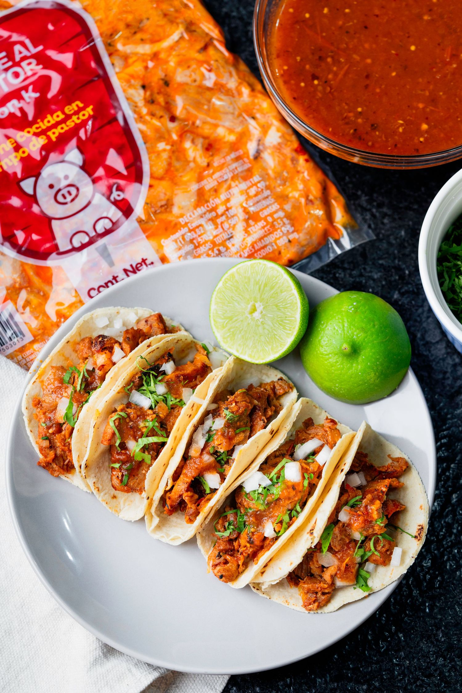 Street tacos topped with fresh cilantro and lime served on white plates with red sauce packets.