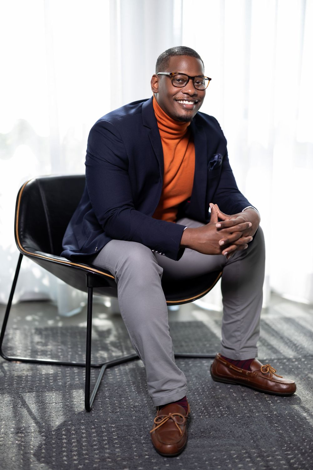 Business professional in blazer and turtleneck seated in modern office setting.