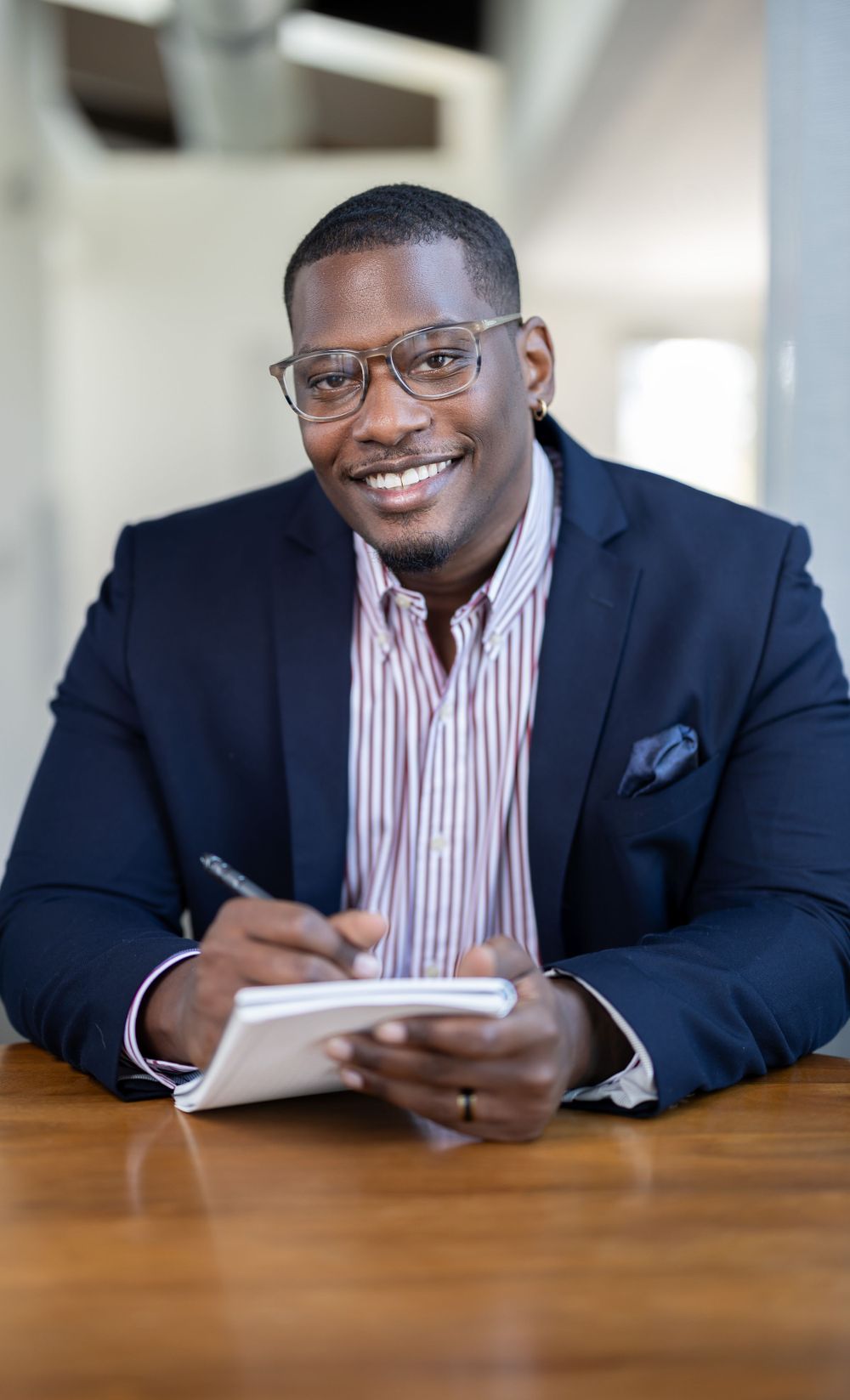 Professional in striped shirt and blazer writing in notebook at desk.
