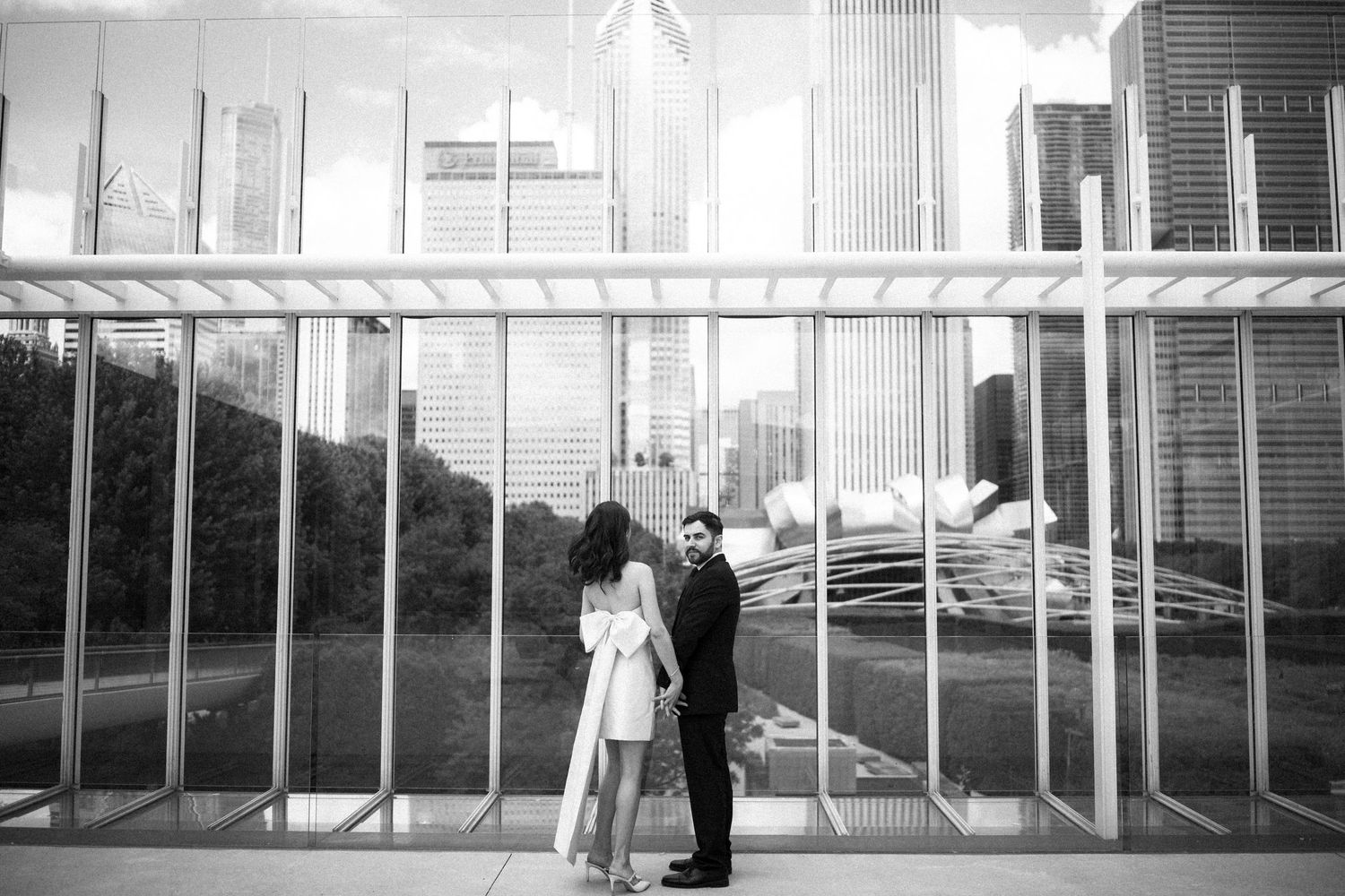 A couple shares an intimate black and white moment outside a mid-century modern building with metal bars.