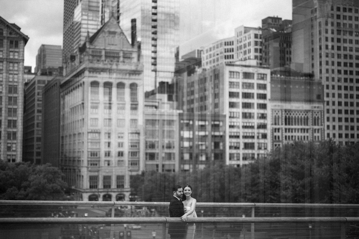 A couple sits together by the reflecting pool overlooking the Manhattan skyline in a black and white photograph.