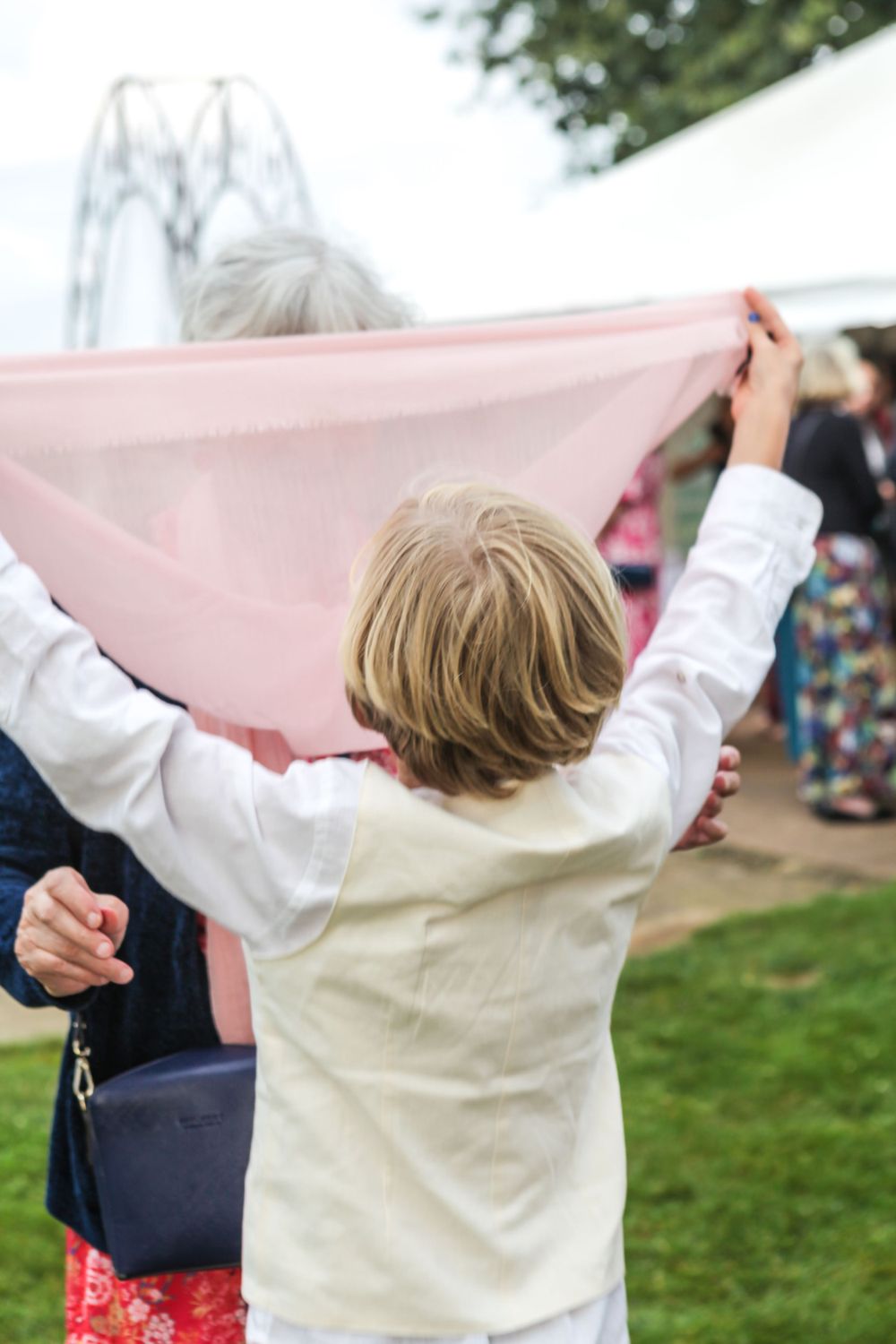 Child holding up pink fabric banner at outdoor event.