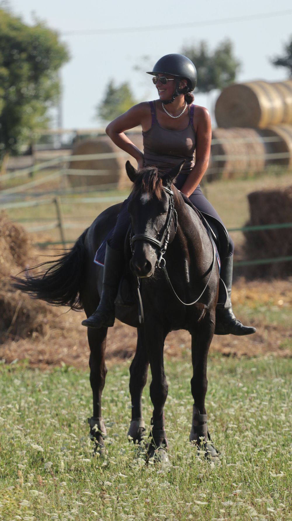 Rider in black helmet and attire practices horseback riding techniques in a grassy field.