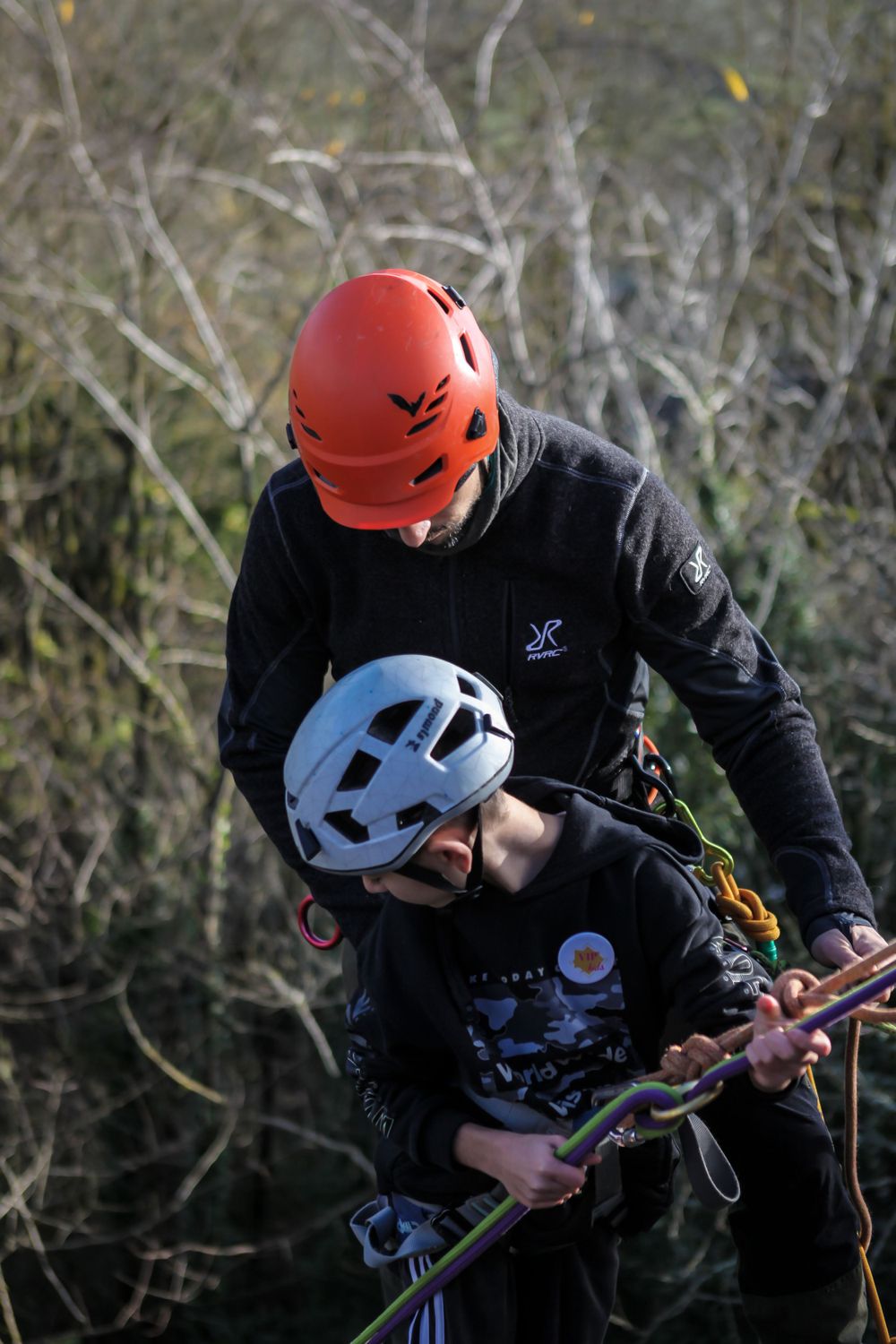 Rock climber wearing orange and blue helmets preparing equipment outdoors.