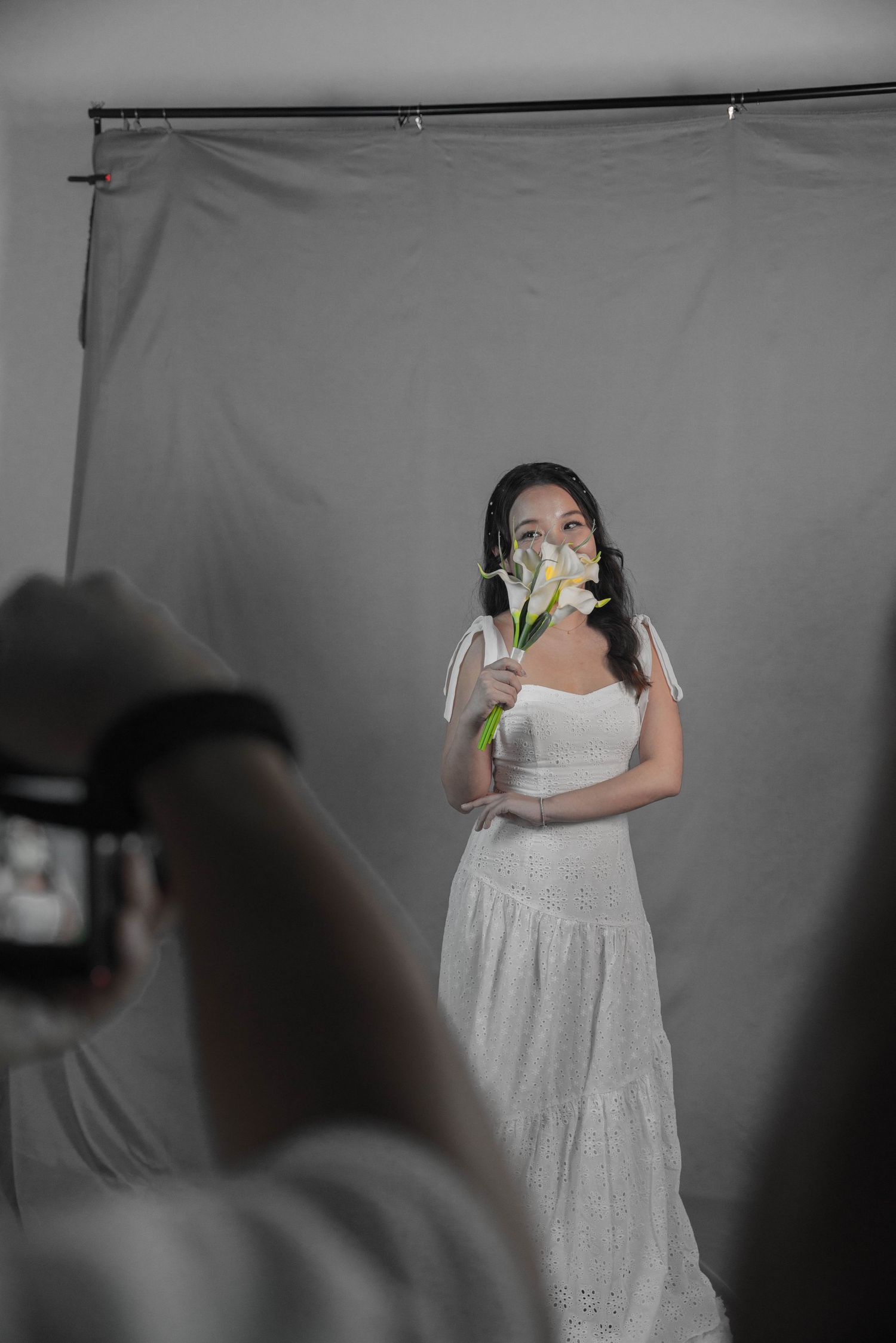 A photoshoot of someone in a white dress holding flowers against a grey backdrop.