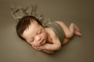 Sleeping newborn in gray wrap against neutral backdrop.