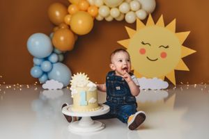 First birthday celebration setup with balloon arch and smiling sun decoration.