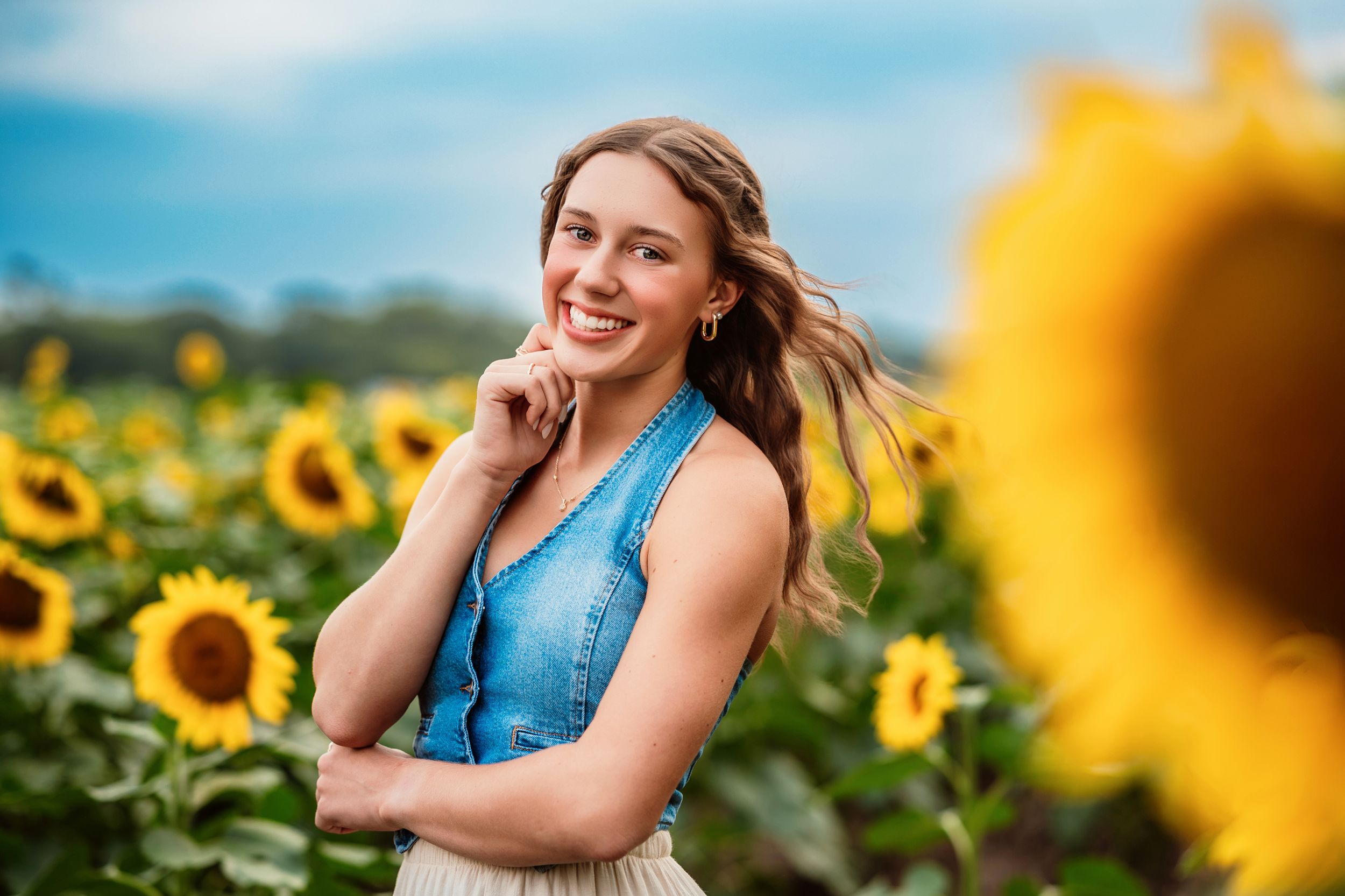 A person poses in a field of bright yellow sunflowers on a sunny summer day with bright blue skies.
