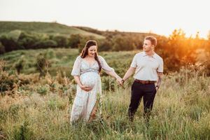 Expecting couple holds hands in scenic field during golden hour maternity photoshoot.