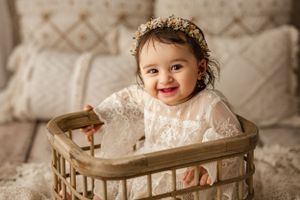 Happy baby in white lace dress sitting in vintage basket.