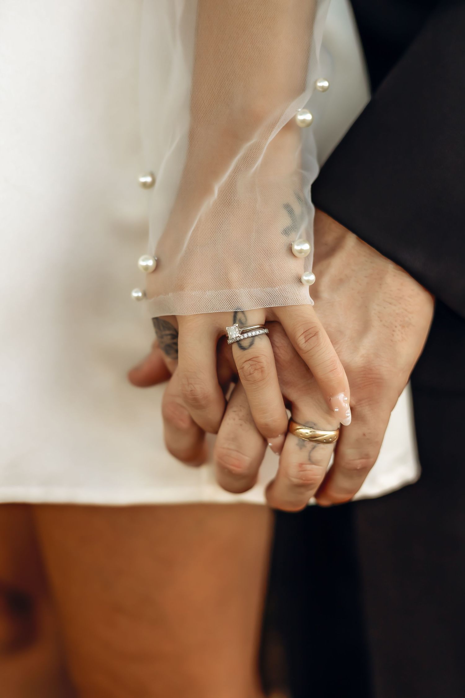 Close up of newlywed couple holding hands showing wedding rings and pearl-decorated veil.