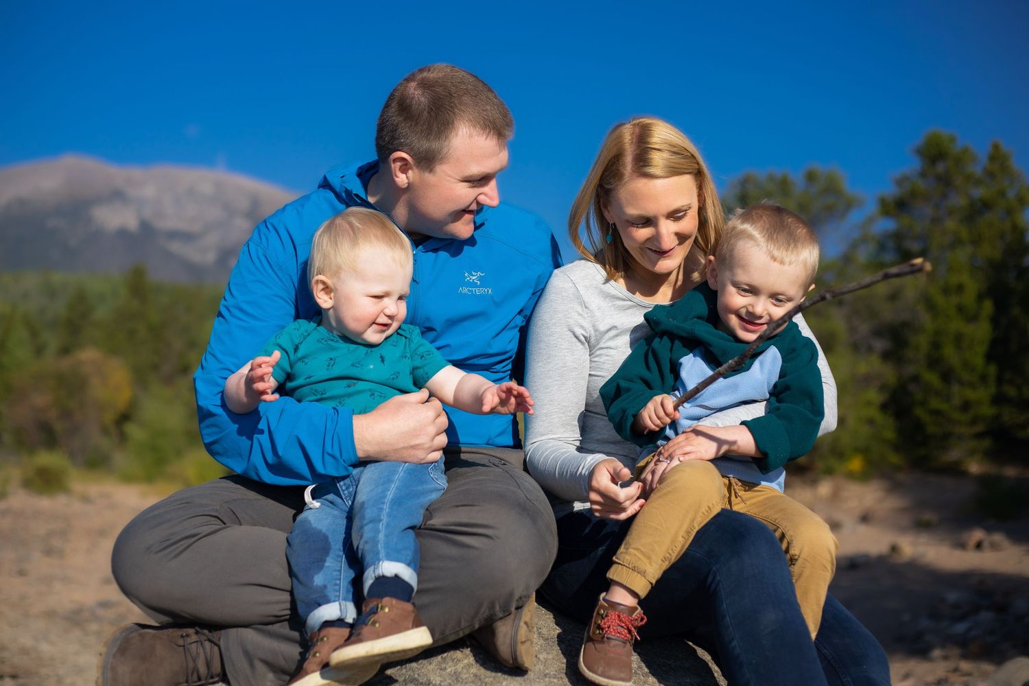 Parents playing their two young sons while sitting on a large rock together