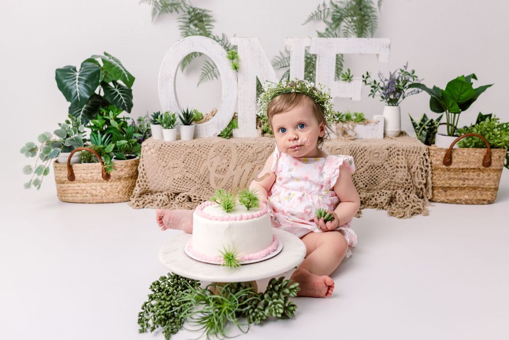 Adorable cake smash photography setup with botanical greenery, wicker baskets and a birthday cake against pink backdrop in cedar park tx