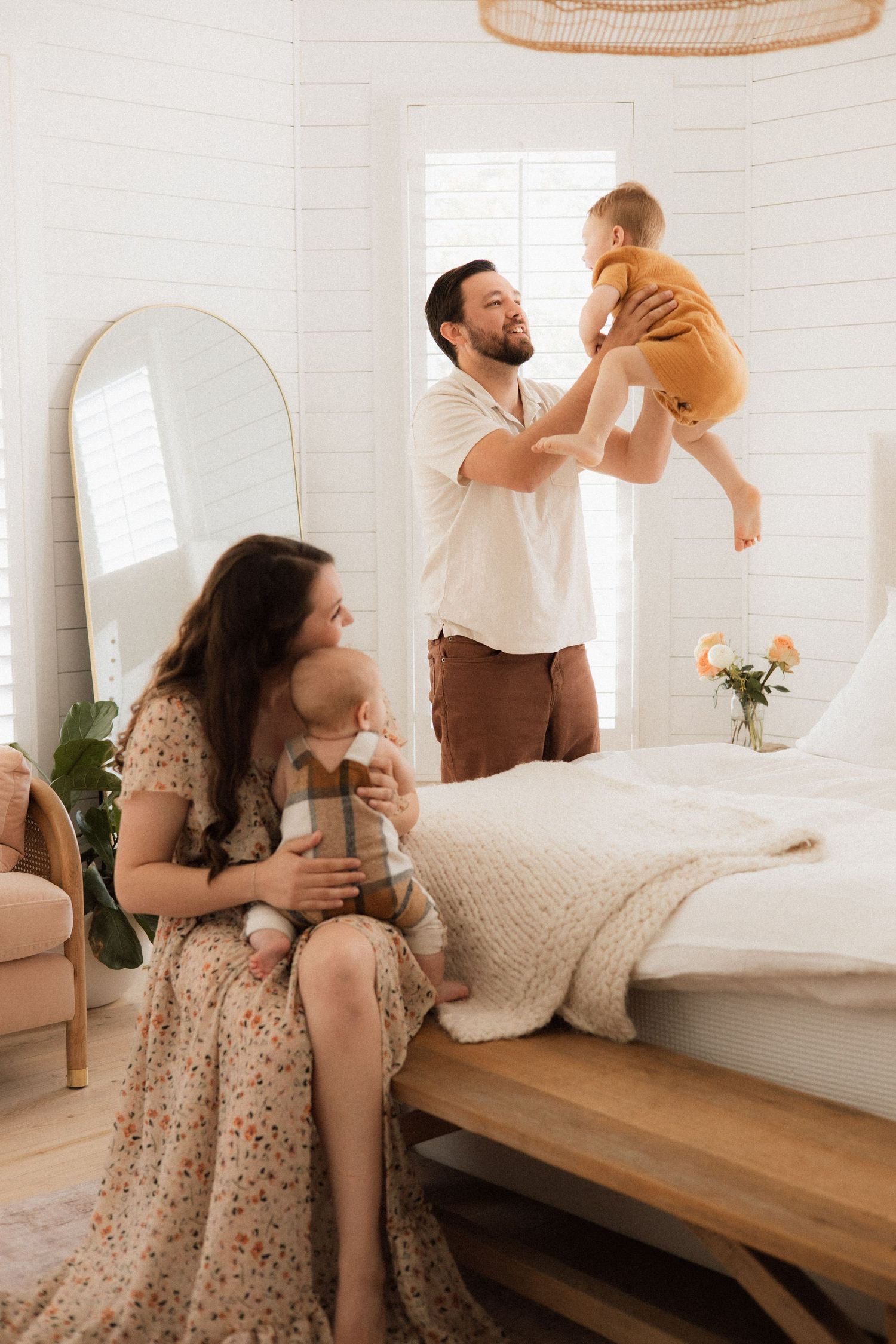 A family sits together on a white couch, sharing a joyful moment as they play with two young children.