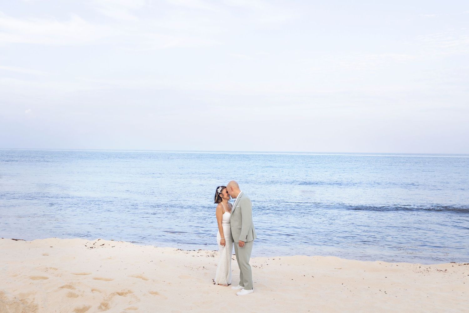 A romantic wedding couple poses in a garden setting framed by lush tropical palm fronds in moody lighting.