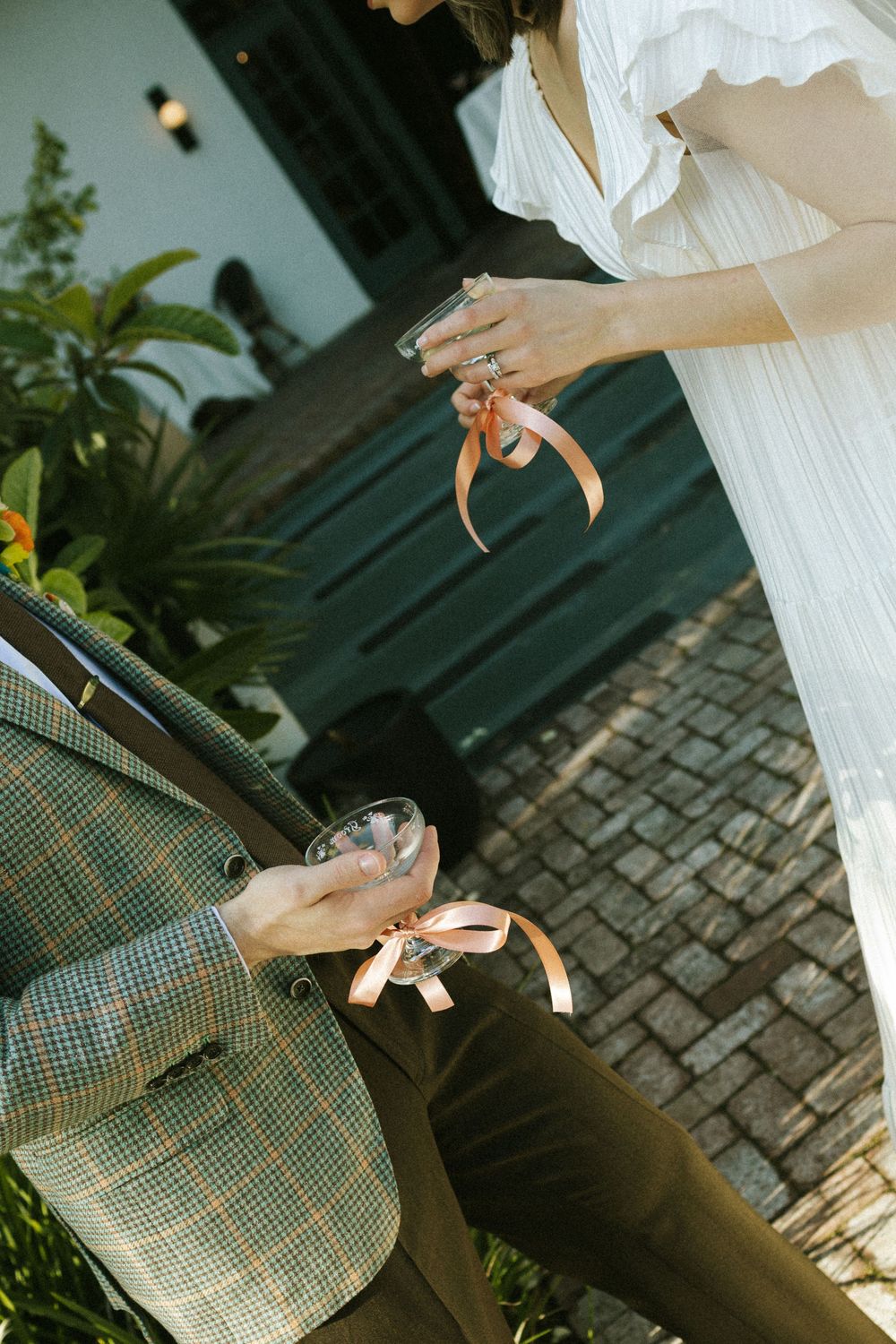 Two people hold champagne glasses wrapped in pink ribbon