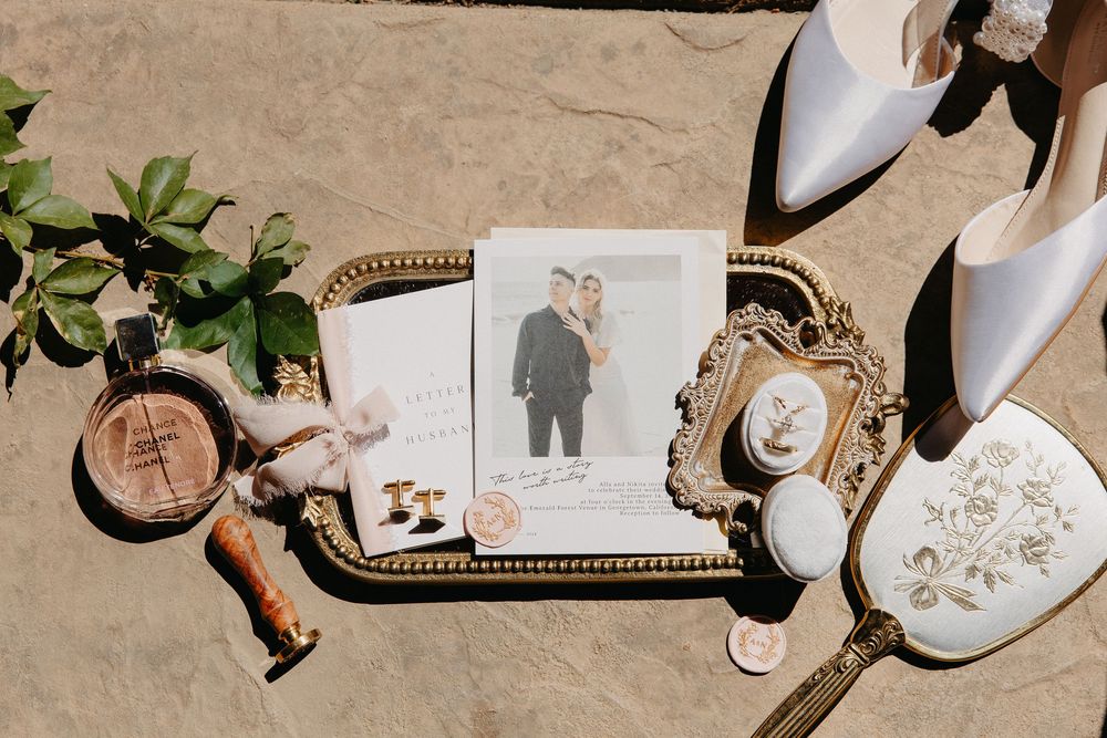Wedding detail flat lay with white shoes, rings, and illustrated wedding stationery on beige background.