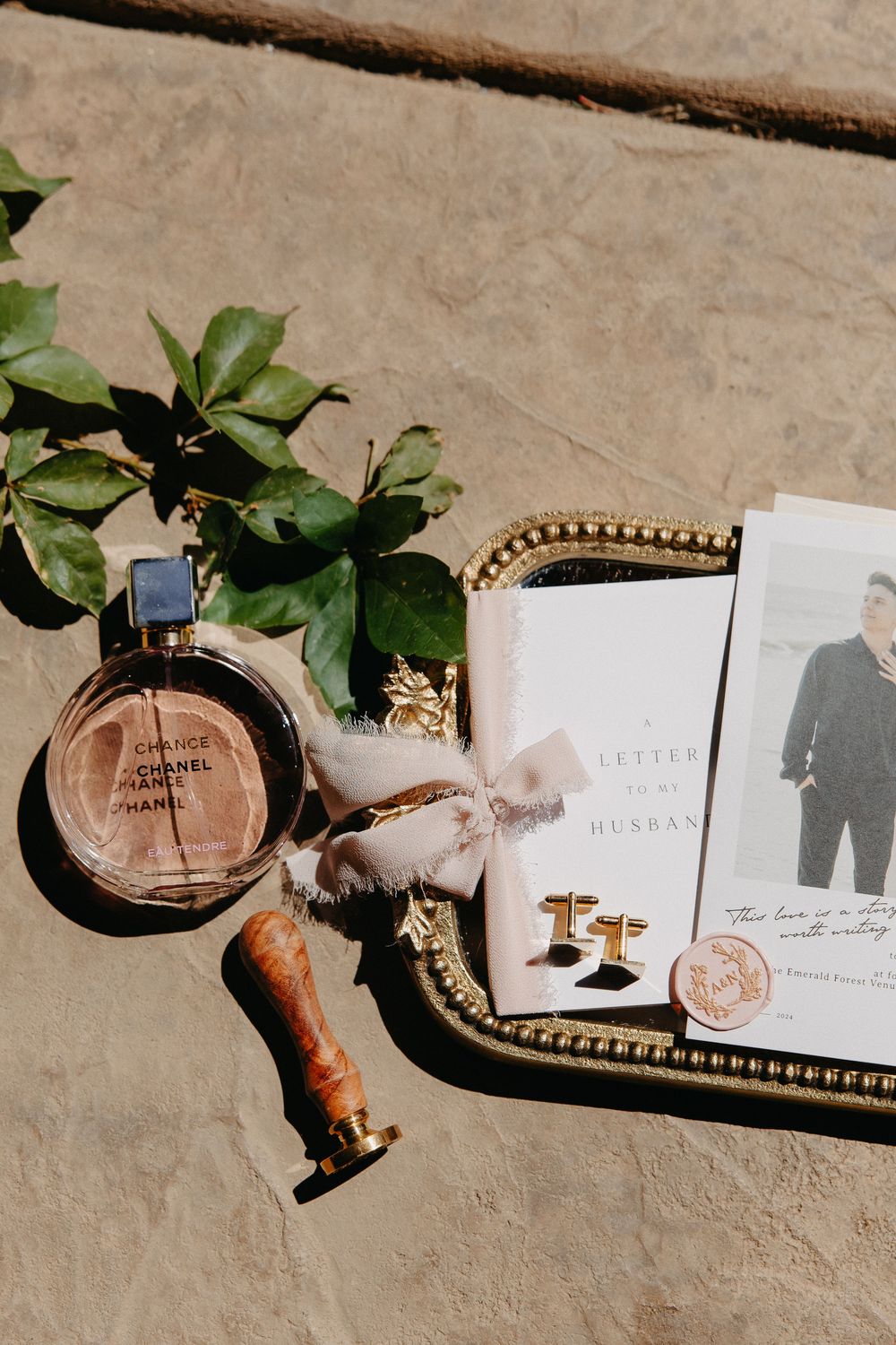 Wedding details flatlay with perfume bottle, wax seal, and photograph on a stone surface.