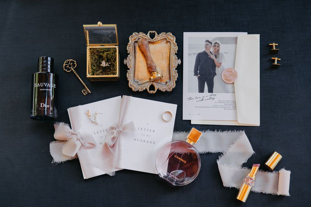 Wedding details flatlay with vintage keys, perfume, invitations and photographs on dark background.