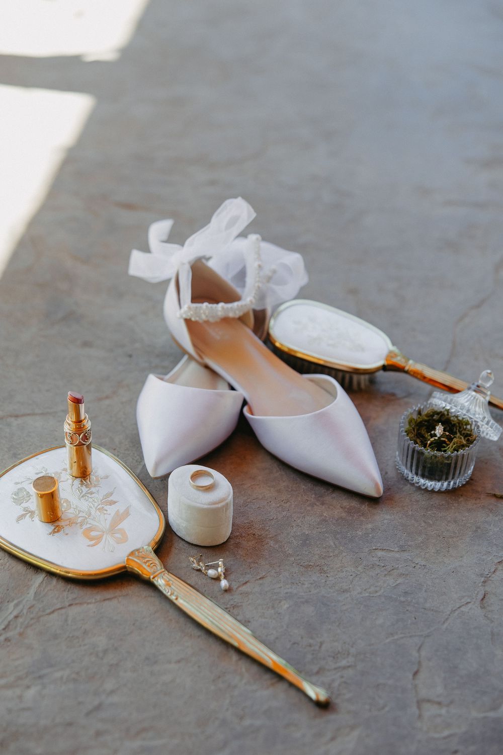 White bridal flats with ribbons displayed alongside vintage-style perfume bottles and accessories.