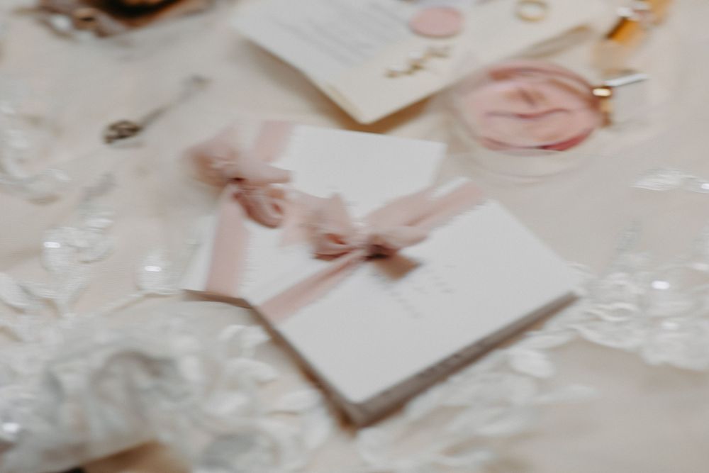Delicate white wedding invitations with soft pink ribbon bows on a lace-decorated table.