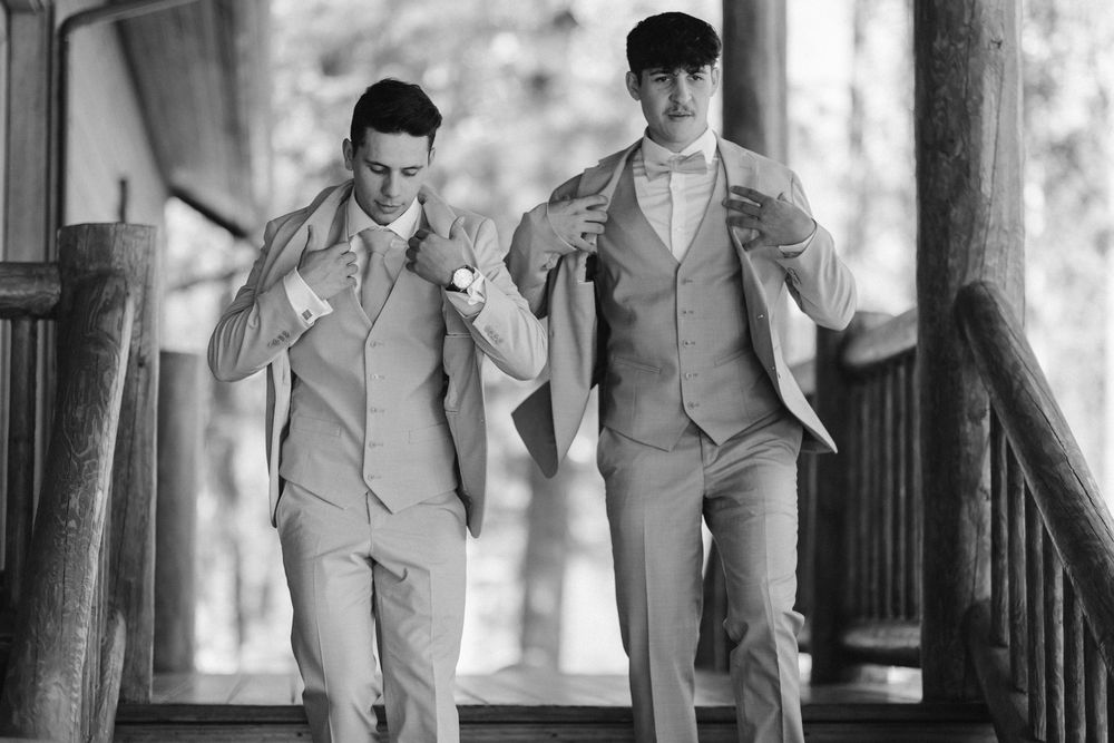 Black and white photo of matching suited couple running joyfully on rustic porch.