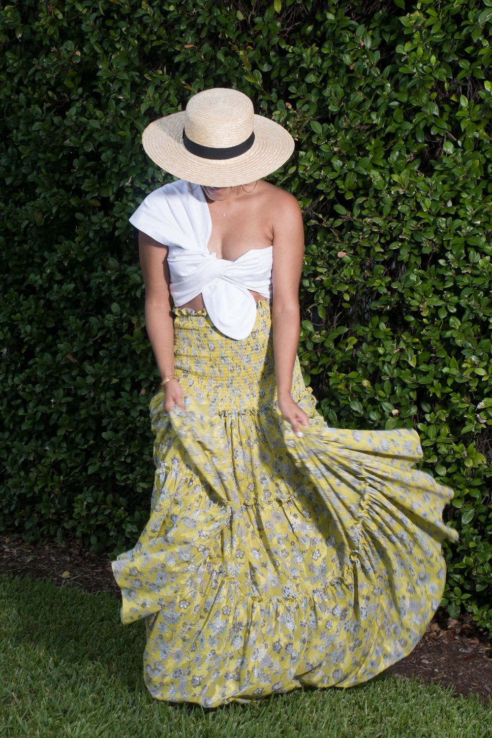 A series of photos showing a yellow floral sundress with a white hat against a lush green garden backdrop.