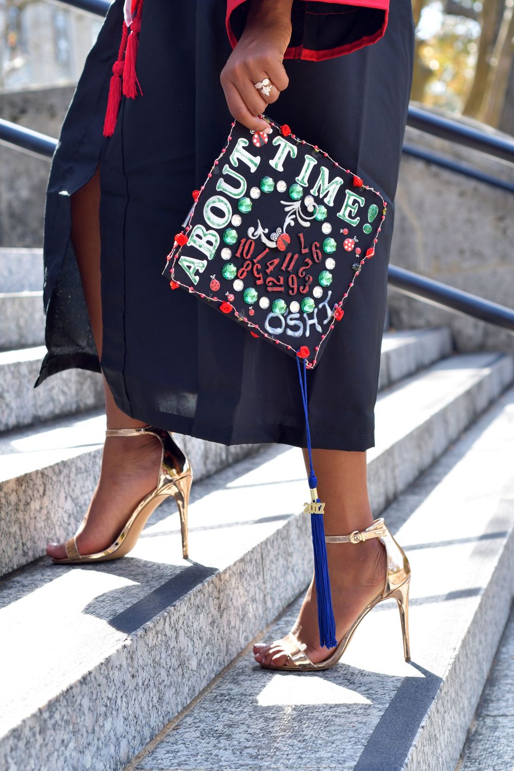 Close-up view of fashionable black and red clutch bag with text design paired with blue and gold high heels on stone steps.