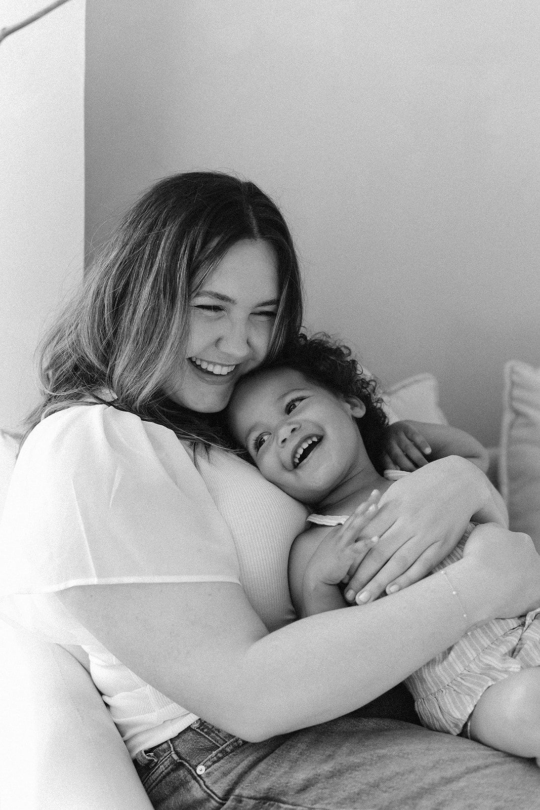 Black and white portrait of loving parent and child laughing and embracing while relaxing together at home.