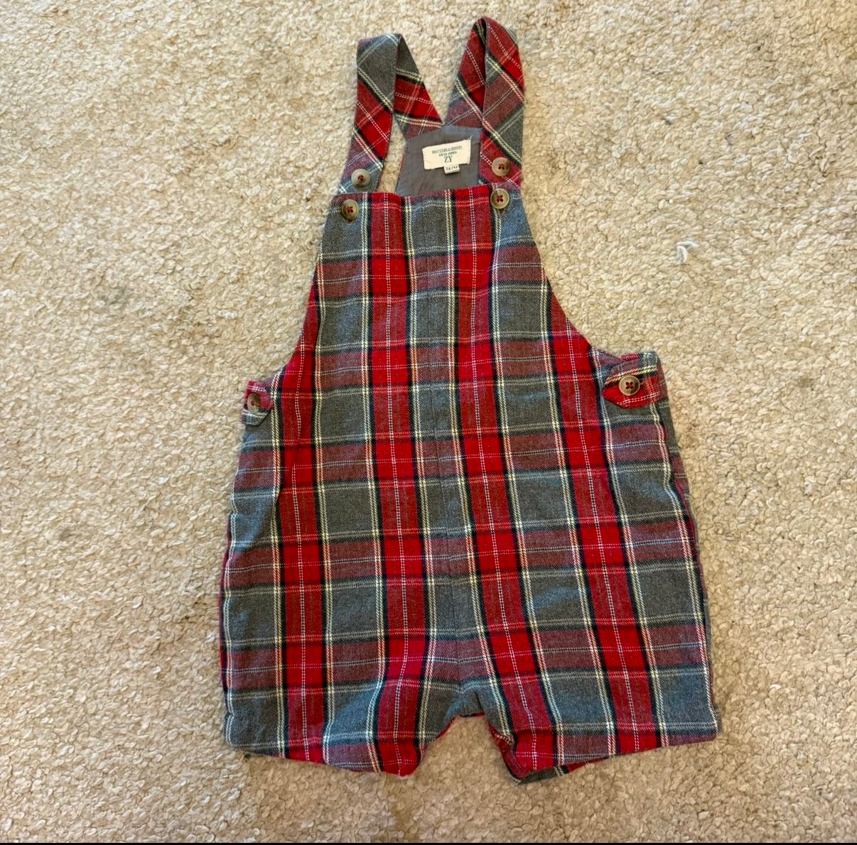 Red and gray plaid baby overalls displayed on carpet.